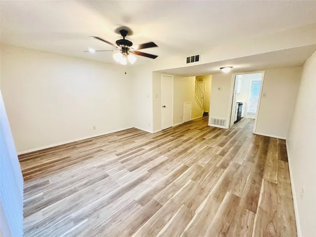 a view of an empty room with wooden floor and a ceiling fan
