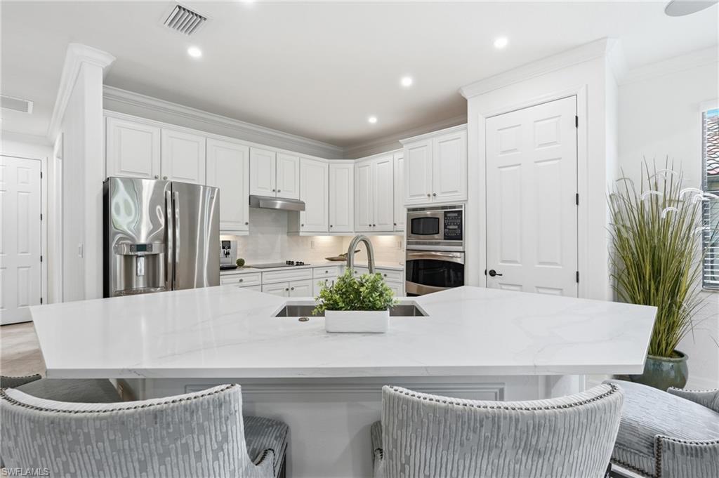 9479 Piacere Way Naples, FL 34113 - Photo 10 of 48 Bright kitchen featuring white cabinetry, stainless steel appliances, a large island with an undermount sink, recessed lighting, and crown molding