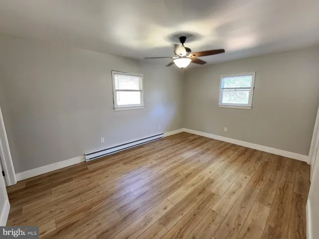 an empty room with wooden floor chandelier fan and windows