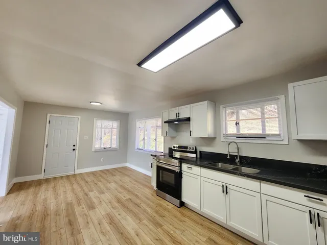 a kitchen with granite countertop a stove a sink and white cabinets