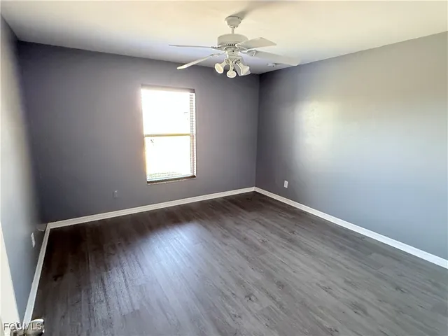an empty room with wooden floor chandelier fan and windows