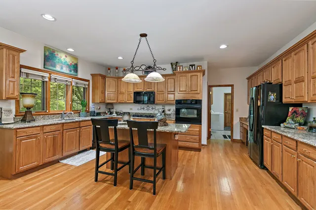 a kitchen with stainless steel appliances kitchen island granite countertop a stove a refrigerator a sink a dining table and chairs with wooden floor