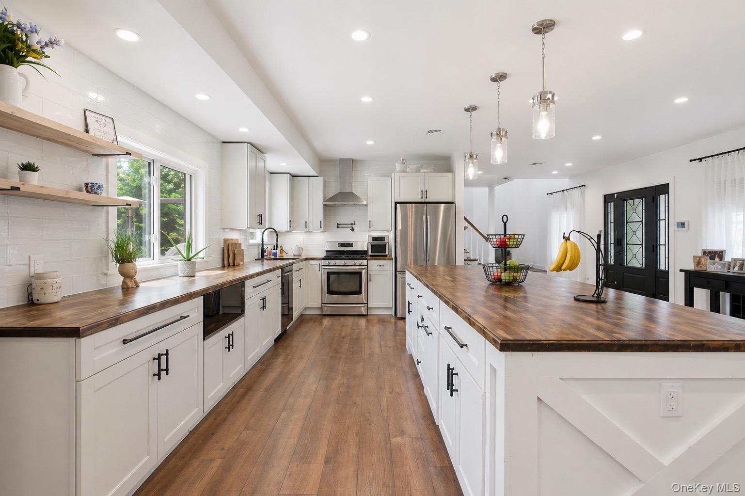 18 Pond Road Holbrook, NY 11741 - Photo 4 of 41 Open-concept kitchen featuring an expansive island with wood-finish countertop, white cabinetry with matte black hardware, stainless steel appliances, and wood-finish flooring