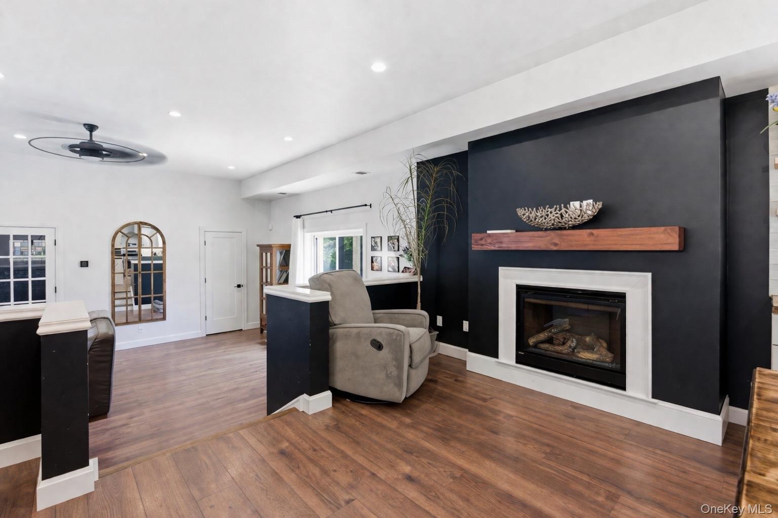 18 Pond Road Holbrook, NY 11741 - Photo 8 of 41 Living area featuring wood-finish flooring, a Gas fireplace with a white mantel and hearth, a dark accent wall, recessed lighting, and a ceiling fan