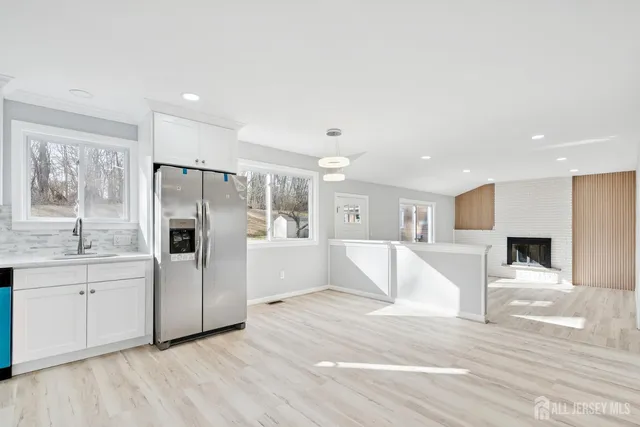 a large white kitchen with a refrigerator a sink dishwasher a stove and white cabinets with wooden floor