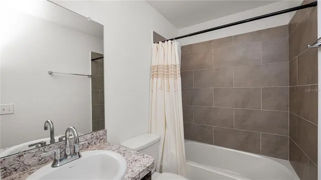 a bathroom with a granite countertop bathtub shower sink vanity and toilet