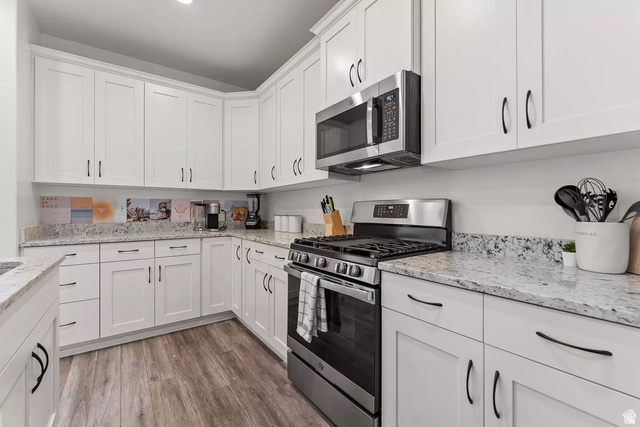 1166 North Riviera Alley Washington, UT 84780 - Photo 7 of 26 Kitchen with stainless steel appliances, white cabinetry, light stone countertops, and light wood-type flooring