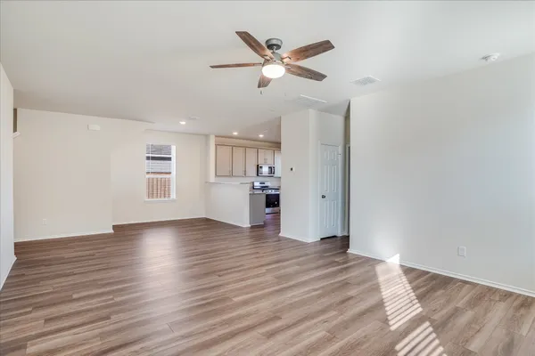 a view of an empty room with wooden floor and a ceiling fan