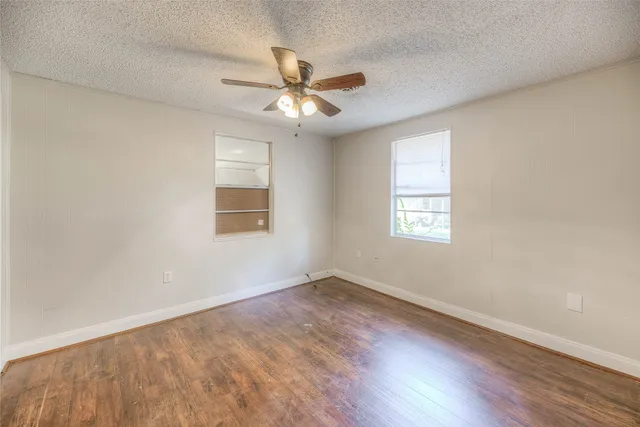 an empty room with wooden floor fan and windows