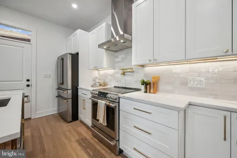 a kitchen with stainless steel appliances granite countertop a stove a refrigerator and a white cabinets with wooden floor