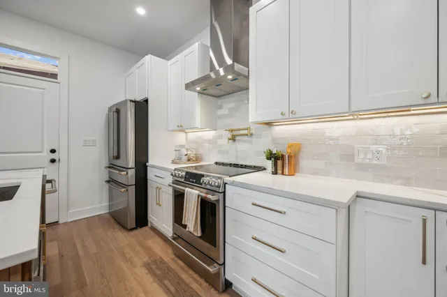 a kitchen with stainless steel appliances granite countertop a stove a refrigerator and a white cabinets with wooden floor