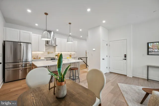 a kitchen with stainless steel appliances granite countertop a refrigerator a sink a stove and a dining table with wooden floor