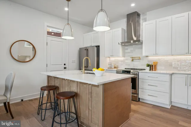 a kitchen with stainless steel appliances a sink a stove a refrigerator and chairs