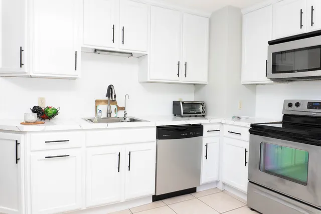 a kitchen with stainless steel appliances kitchen island granite countertop a sink a stove a refrigerator and white cabinets