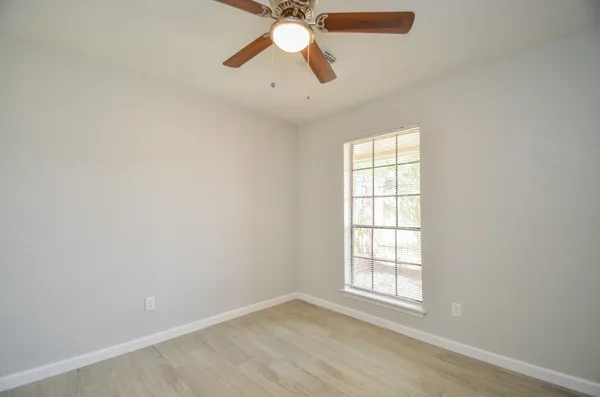 an empty room with chandelier fan and windows