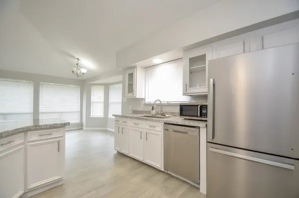a kitchen with stainless steel appliances granite countertop a refrigerator a sink dishwasher a stove with white cabinets and wooden floor