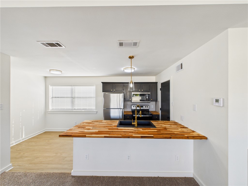 309 Mobile Avenue, Unit 6 Bryan, TX 77801 - Photo 5 of 12 Kitchen featuring a peninsula, appliances with stainless steel finishes, butcher block counters, decorative light fixtures, and light carpet