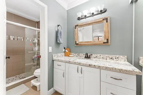 a bathroom with a granite countertop sink a toilet a mirror and shower