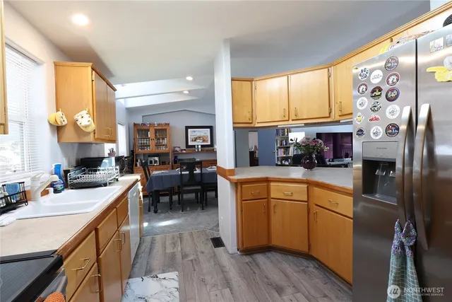 a kitchen with stainless steel appliances granite countertop a refrigerator a sink dishwasher a stove and a dining table with wooden floor