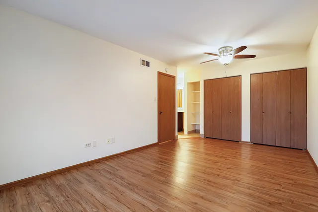 a view of an empty room with wooden floor and ceiling fan