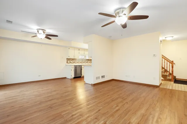 an empty room with wooden floor chandelier fan and windows