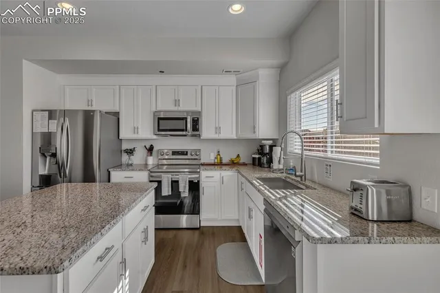 a kitchen with granite countertop a sink stainless steel appliances and white cabinets