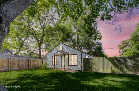 a view of a yard in front of a house with plants and large trees