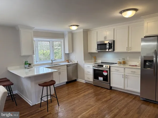 a kitchen with stainless steel appliances a stove a sink a refrigerator and white cabinets with wooden floor