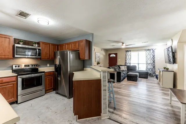 a living room with stainless steel appliances kitchen island granite countertop a refrigerator a stove top oven a sink dishwasher and wooden cabinets