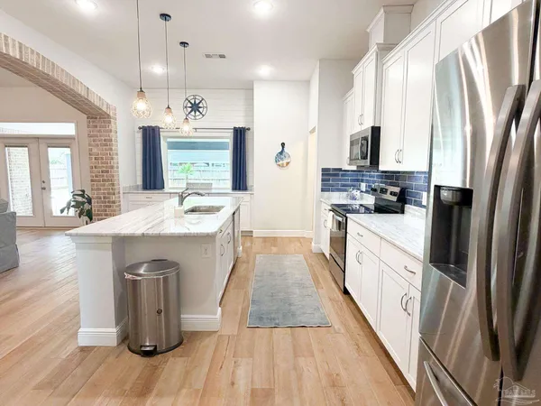 a large kitchen with stainless steel appliances a stove a sink dishwasher a refrigerator white cabinets and wooden floor