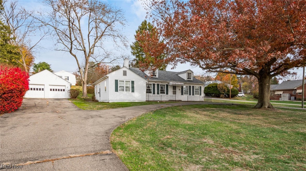 New england style home with a front lawn, an outdoor structure, a garage, and covered porch
