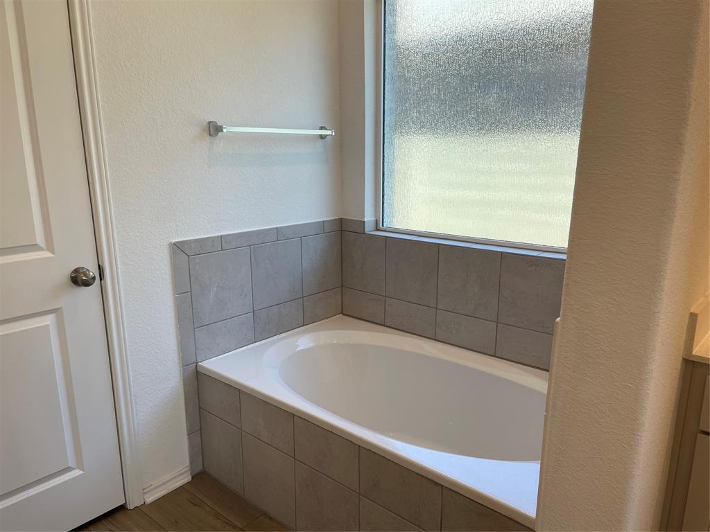 129 Starflower Cove Georgetown, TX 78628 - Photo 16 of 31 Bathroom with a garden tub, vanity, a textured wall, and light wood-style flooring