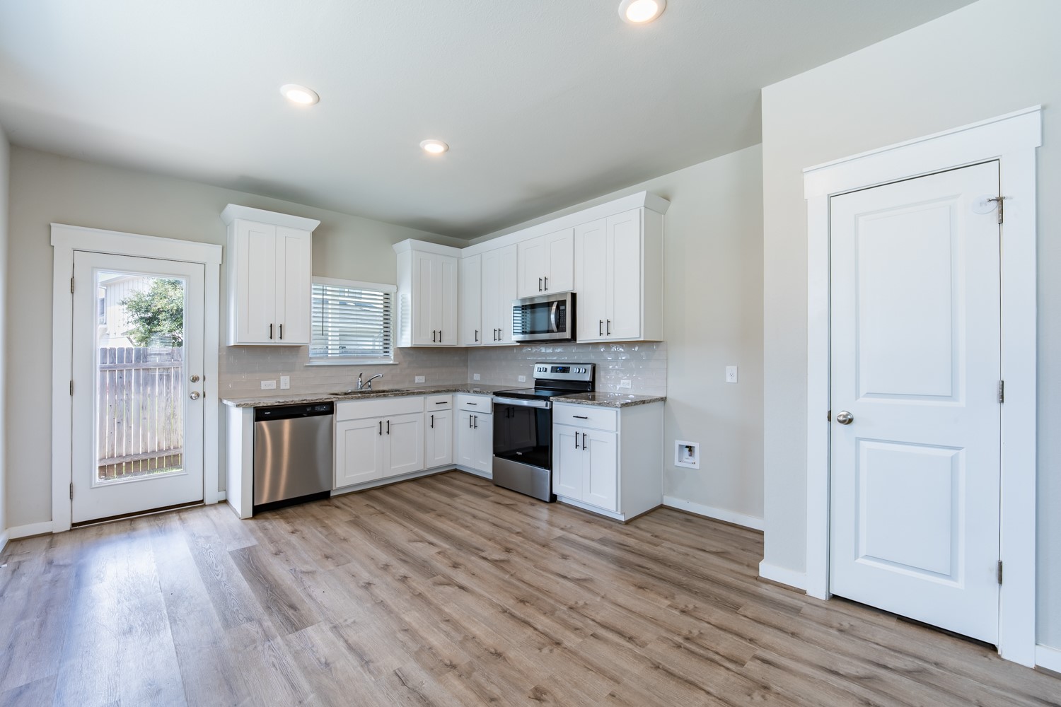 147 Waterside Road, Unit A Buda, TX 78610 - Photo 11 of 27 A well-lit kitchen with sleek stainless steel appliances, crisp white cabinetry, and durable hardwood flooring.
