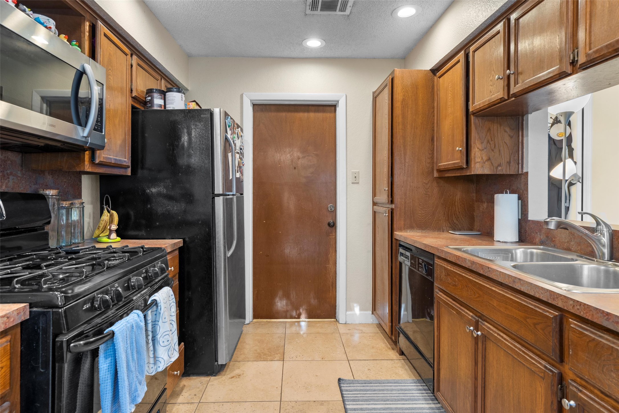 6492 Hart Lane Austin, TX 78731 - Photo 7 of 22 Kitchen featuring black appliances, brown cabinetry, light tile patterned floors, a textured ceiling, and light countertops