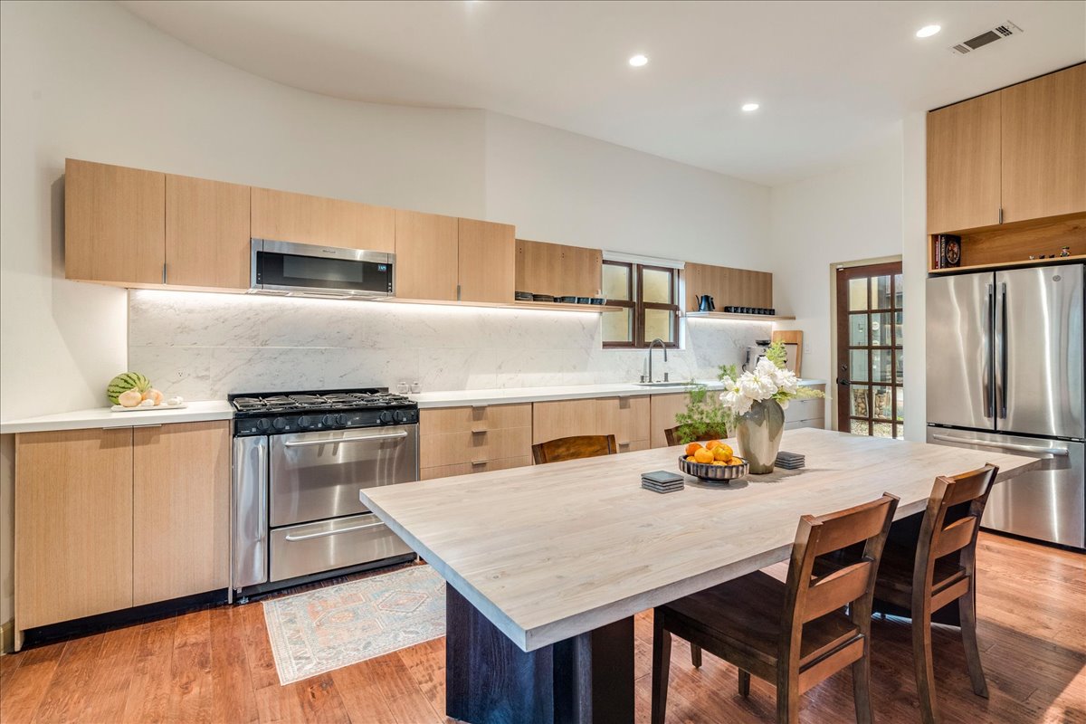 3012 South 4th Street, Unit B Austin, TX 78704 - Photo 8 of 40 Modern kitchen featuring light wood-finish cabinetry, stainless steel appliances, a white stone countertop, and a full-height marble-look backsplash with under-cabinet lighting