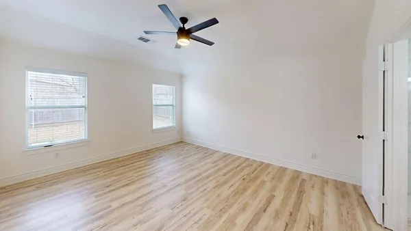 an empty room with wooden floor fan and windows