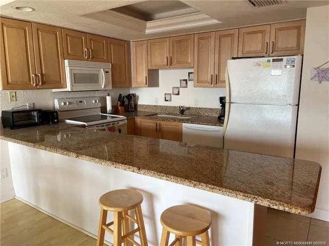 a kitchen with granite countertop a sink a stove a refrigerator a counter top space and cabinets