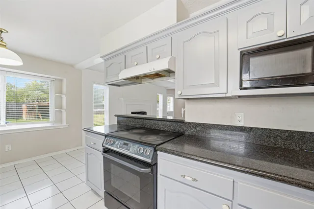 a kitchen with stainless steel appliances granite countertop white cabinets and a stove a window