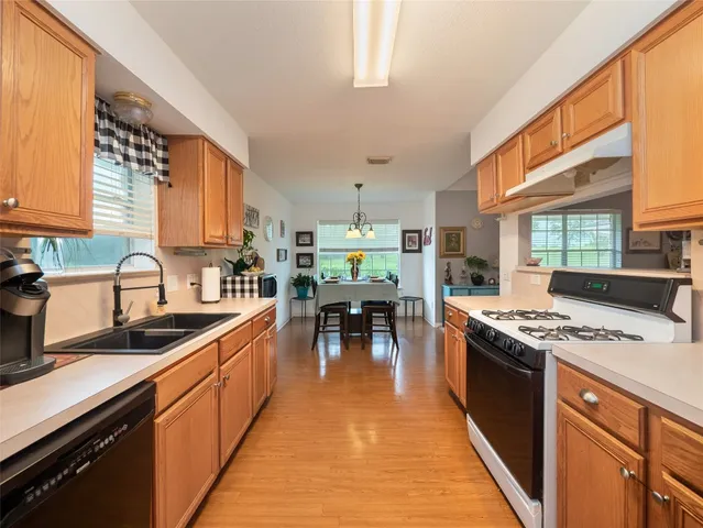 a kitchen with stainless steel appliances granite countertop a stove top oven a sink dishwasher a dining table and chairs with wooden floor