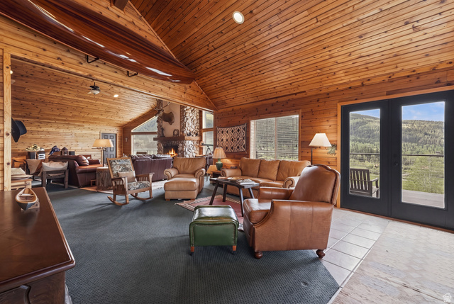 6 Beaver Springs Rancheros Oakley, UT 84055 - Photo 14 of 68 Vaulted wood-paneled ceiling with exposed wood beams, featuring a stone fireplace, large windows, and double glass panel doors opening to a balcony