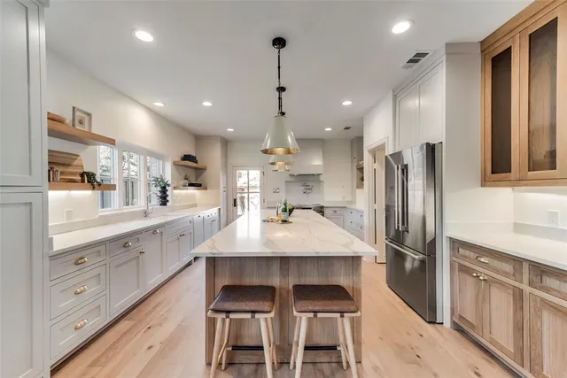 a kitchen with stainless steel appliances kitchen island granite countertop a refrigerator a sink dishwasher and white cabinets with wooden floor