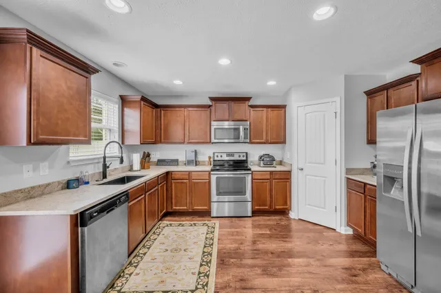 a kitchen with stainless steel appliances granite countertop a refrigerator a sink dishwasher a stove with wooden cabinets and floor