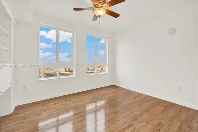 an empty room with wooden floor fan and windows