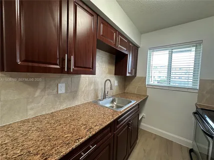 a kitchen with granite countertop stainless steel appliances a sink window and cabinets