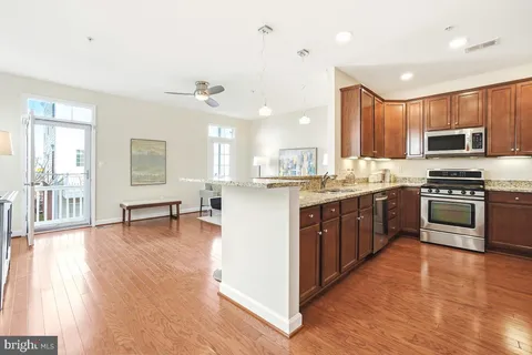 a kitchen with stainless steel appliances a stove a sink dishwasher a microwave oven and a dining table with wooden floor