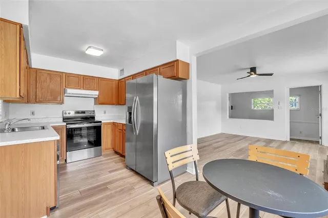 a kitchen with stainless steel appliances granite countertop a refrigerator a stove a sink a dining table and chairs with wooden floor