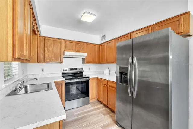 a kitchen with stainless steel appliances granite countertop a refrigerator a sink a stove and white cabinets with wooden floor