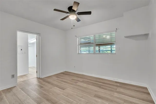 an empty room with wooden floor ceiling fan and windows