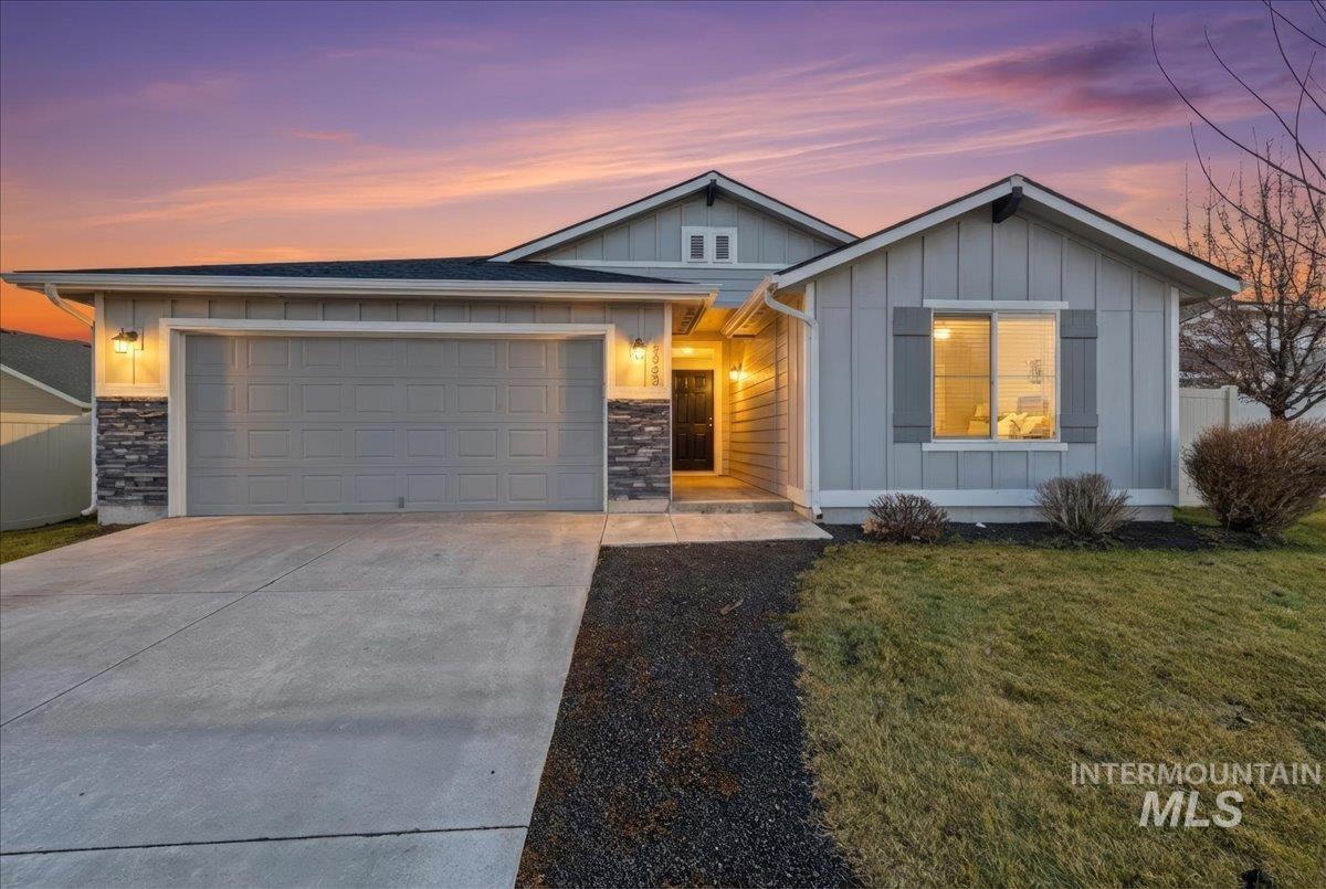 View of front of home with board and batten siding, driveway, stone siding, and a lawn