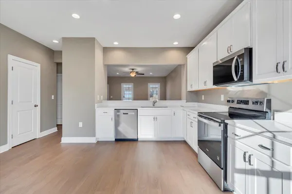a kitchen with stainless steel appliances a stove top oven a sink a refrigerator white cabinets and wooden floor